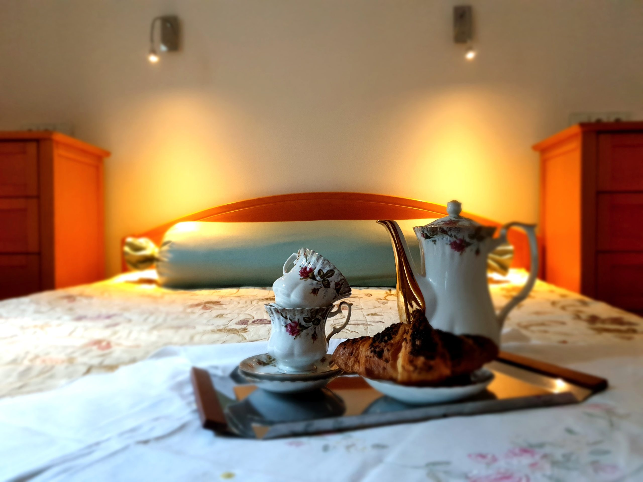 A photograph of a bed with high-end linen and a breakfast in bed set in the forefront with china and croissant